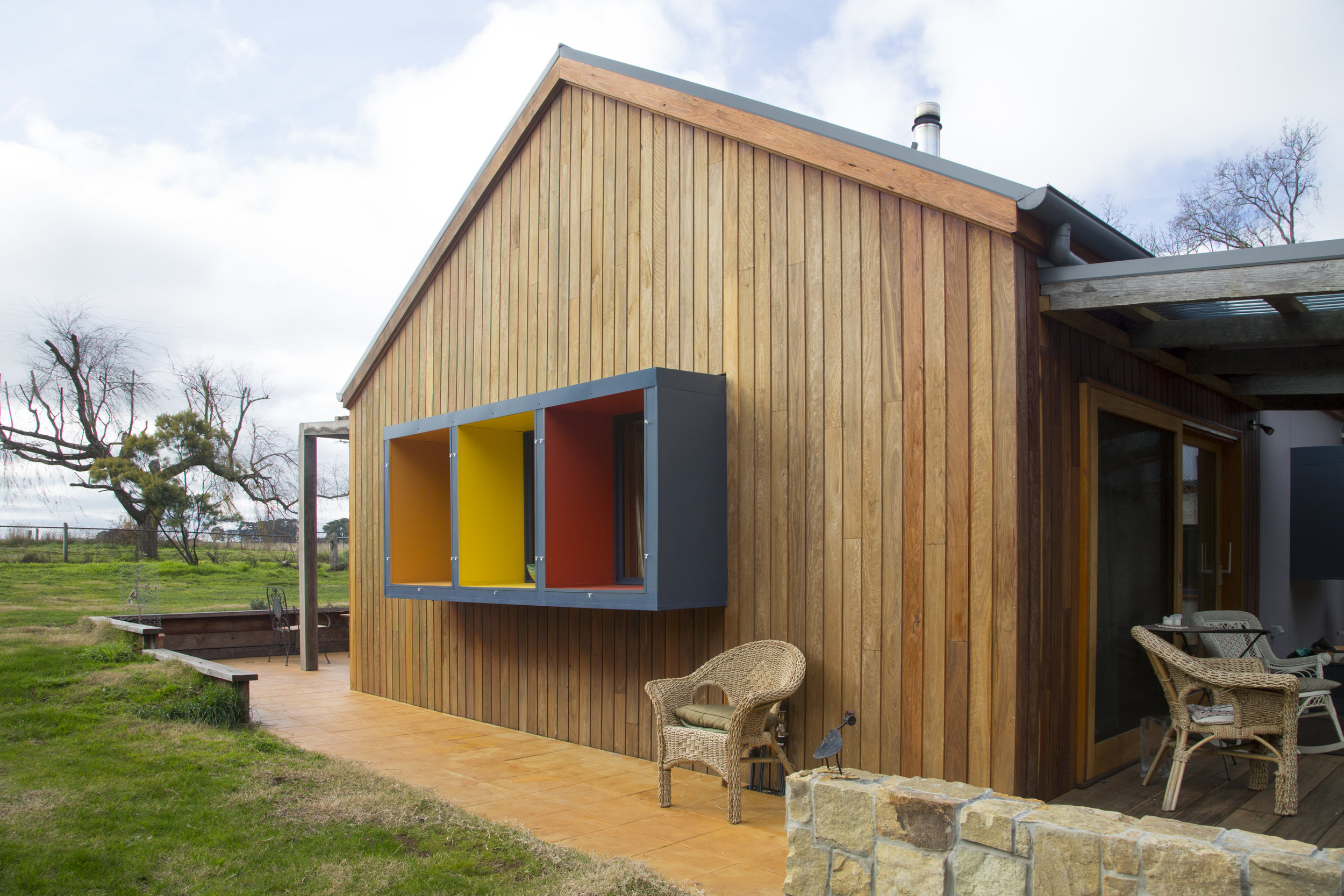 A modern home exterior with bold, bight window frames and stained wood facade designed by Enduring Domain Architecture