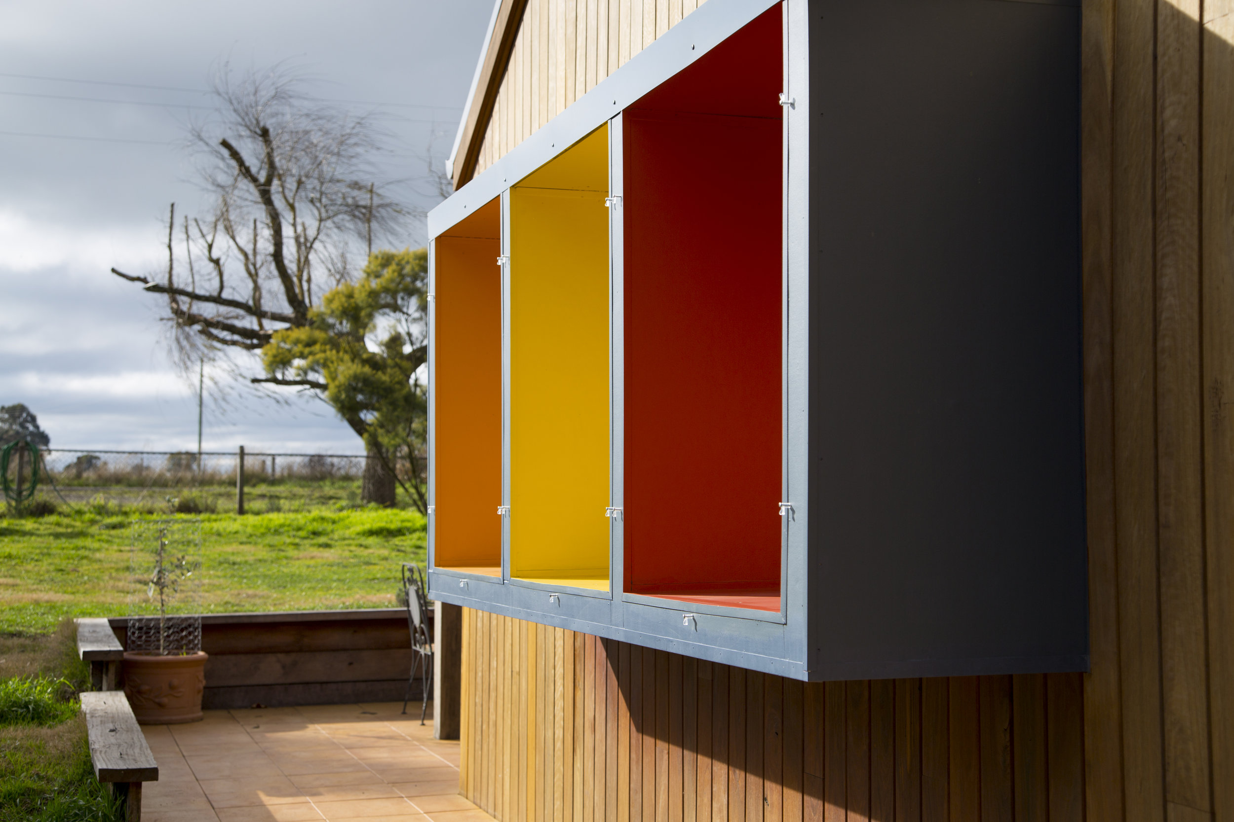 A modern home exterior with bold, bight window frames and stained wood facade designed by Enduring Domain Architecture